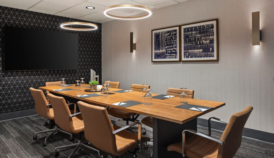 Executive boardroom with a long wood table, leather chairs, geometric accent wall, ring pendant lighting, and a large presentation screen